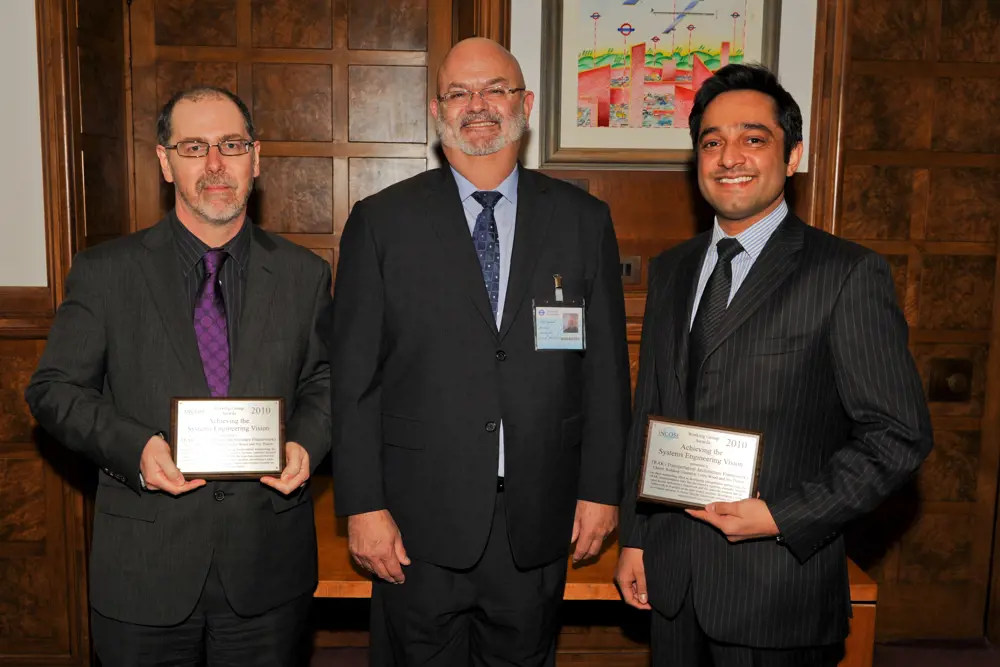 Three men posing for a photo. The ones on the left and right are holding awards.