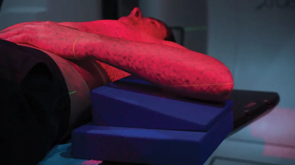 A patient lying down with red light covering their body to accurately position radiotherapy treatment. 