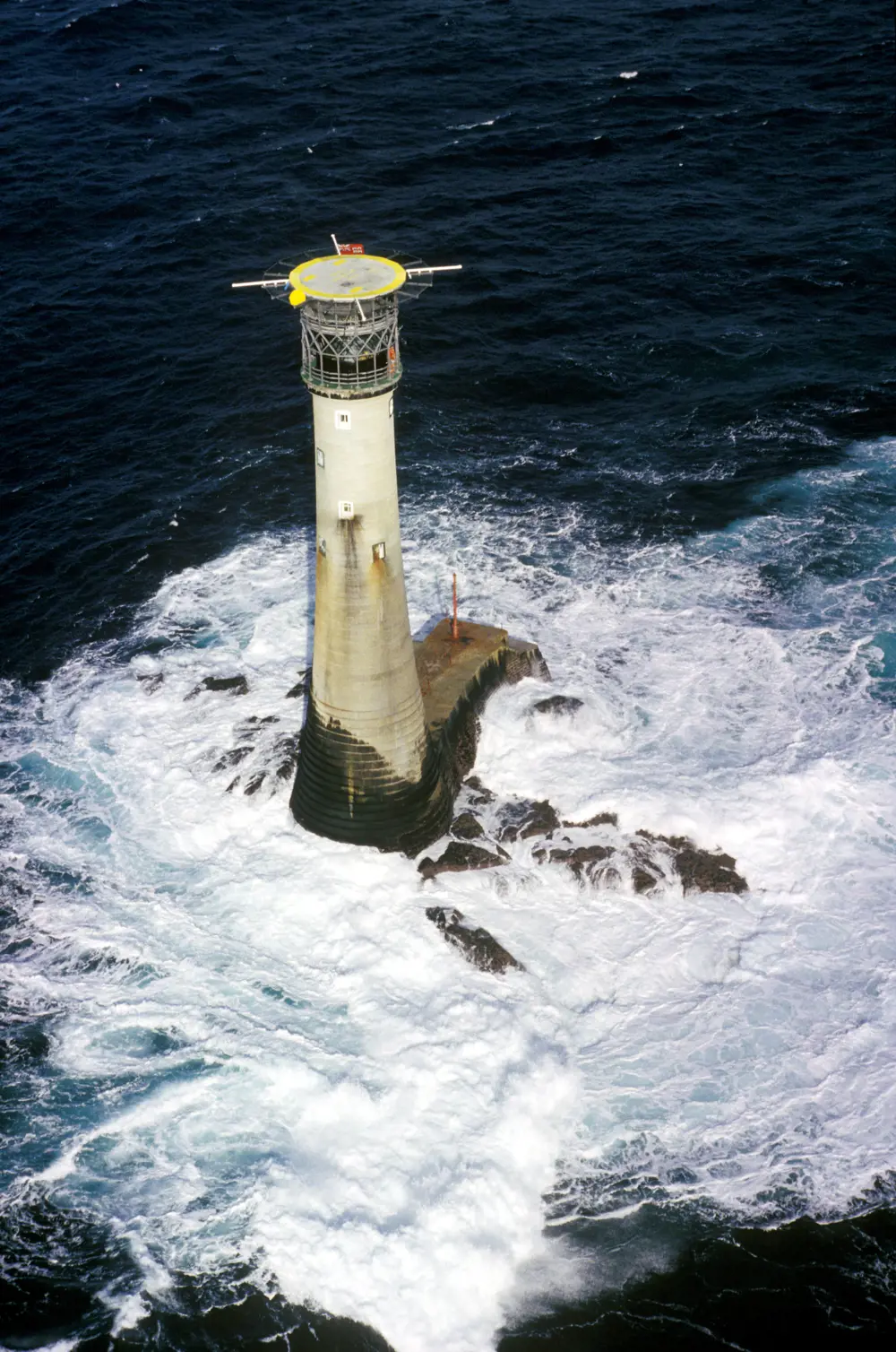 A lighthouse viewed from above. The lighthouse is surrounded by swirling water and topped with a helipad.