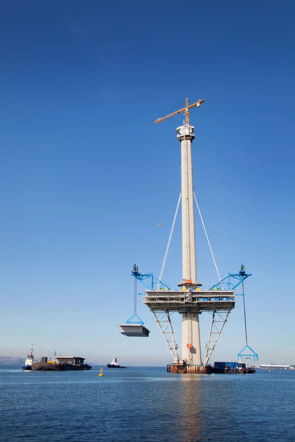Cranes lifting deck sections onto a concrete tower in water. 