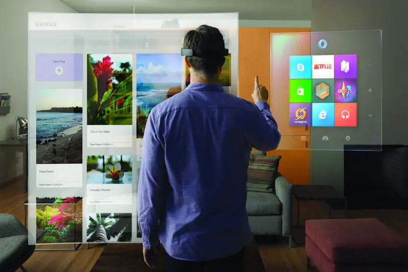 The back of a person wearing a virtual reality headset in a living room, looking at a virtually-generated screen, containing different applications and photos.