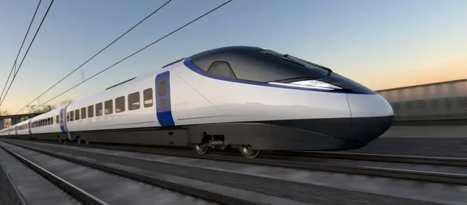 Artist’s impression of a sleek, modern high-speed train traveling on railway tracks. The train has a streamlined design with a pointed nose, white body, and blue accents around the doors. Overhead electric wires run above the tracks, and the background shows a blurred landscape under a clear sky at sunset, suggesting speed and motion.