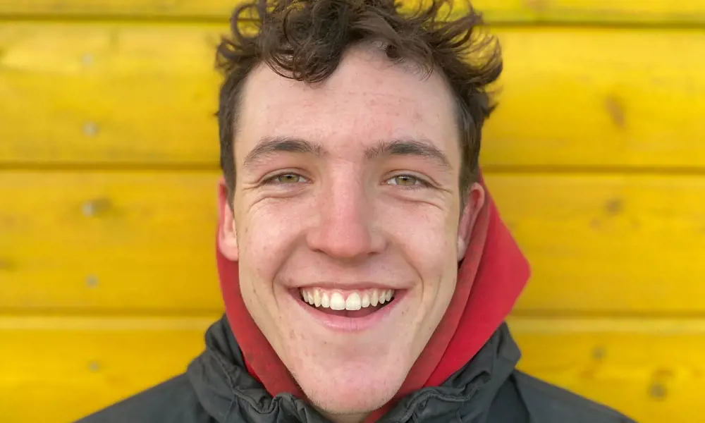 A playground engineer smiling, standing in front of a yellow wall.