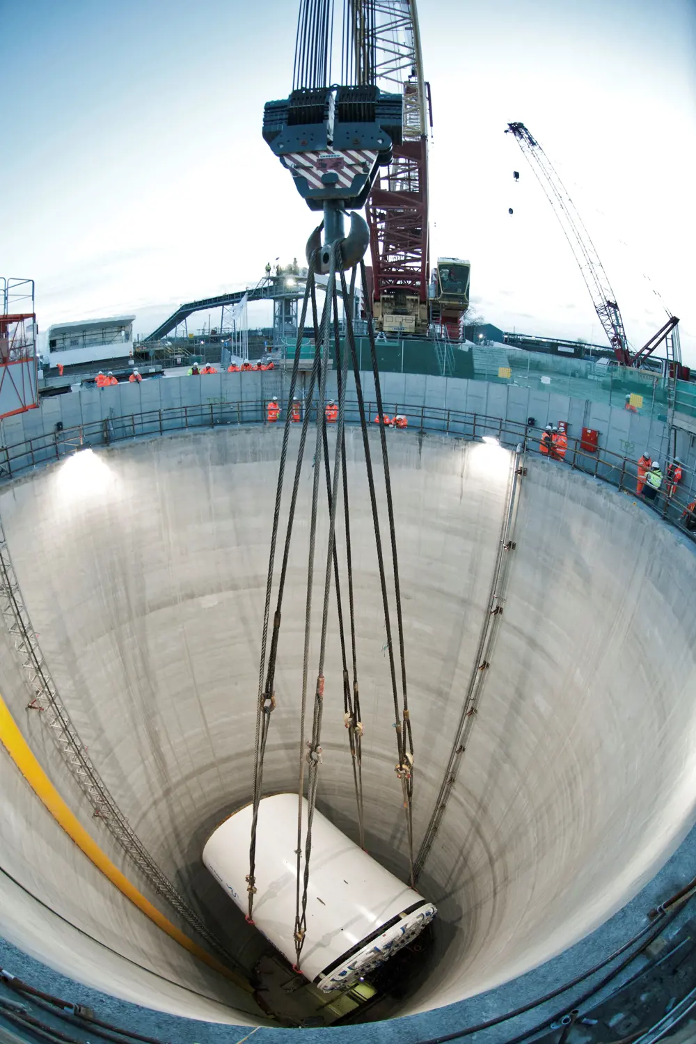 A Tunnel Boring Machine cutter suspended from a crane in the air, being lowered into the Beckton overflow shaft. 