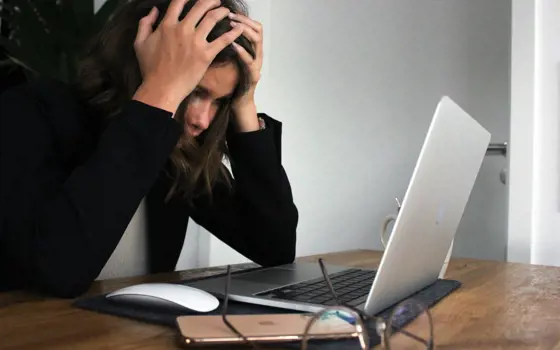 A woman in black long sleeve shirt covering her face with her hands.