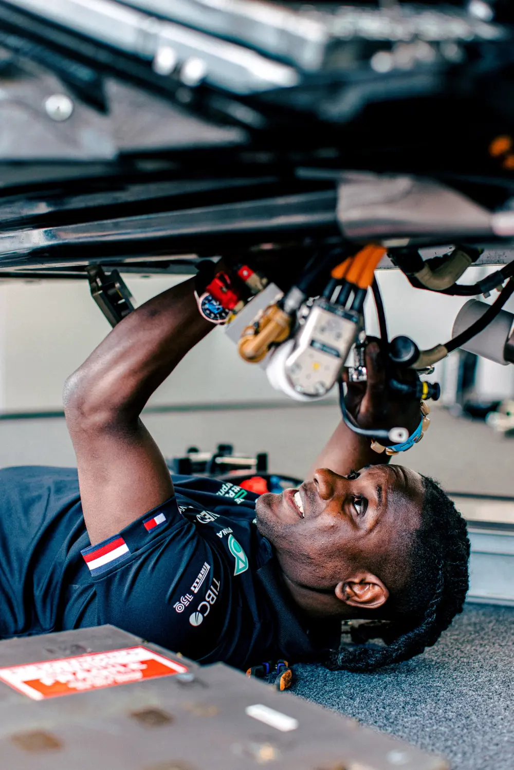 James Dornor lies beneath a car, working on components above him with a tool.