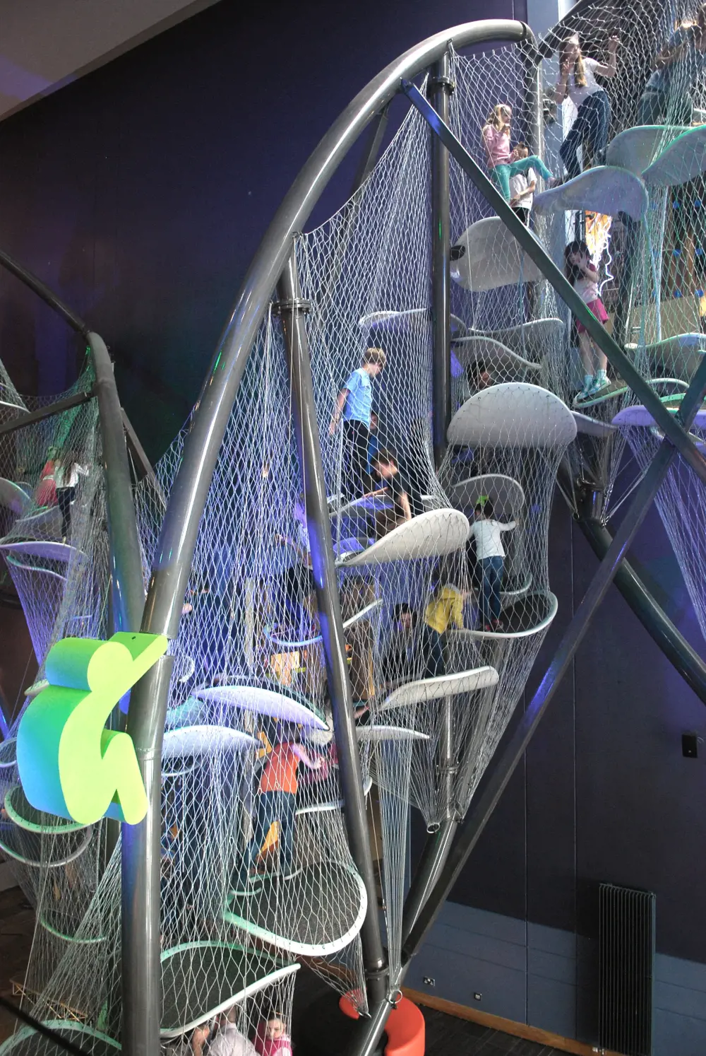 Children climb on a climbing frame made from ovals arranged in space surrounded by mesh