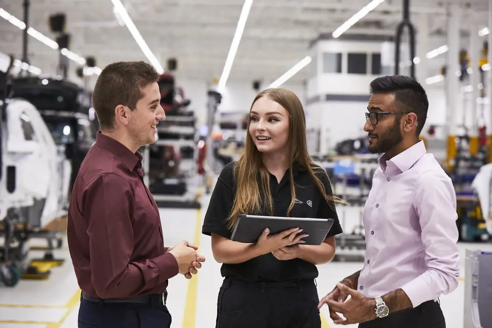 Three apprentices talking to each other inside a factory.