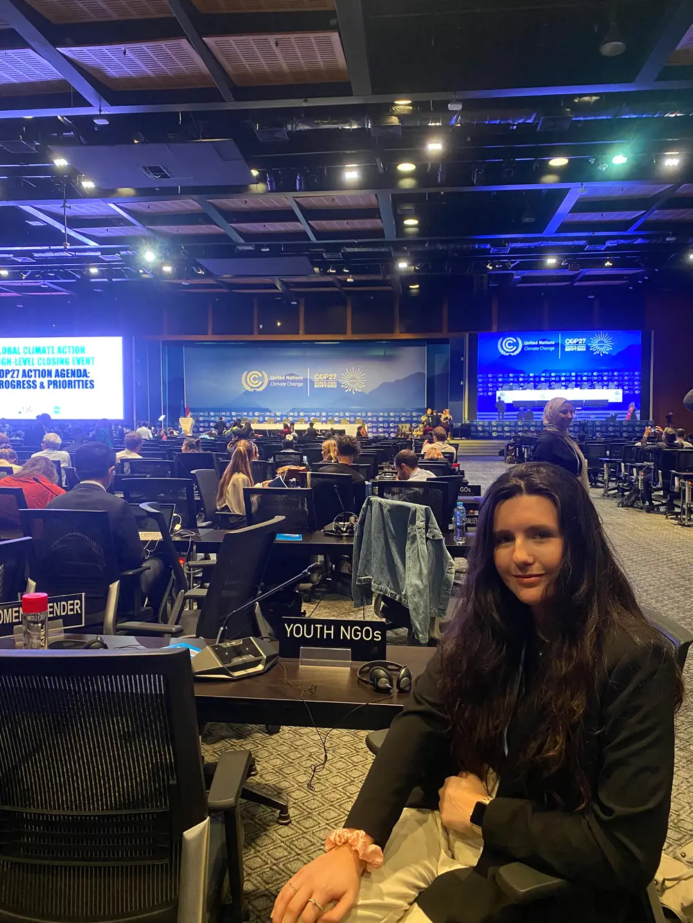 A woman sitting at a desk in a conference room. There is a sign that says "Youth NGOs" in front of her