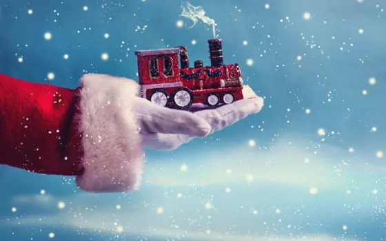 A hand with a red and white fluffy sleeve and white glove holding a toy train with steam coming out the top.