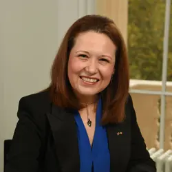 A woman wearing a blue shirt and black jacket smiles at the camera