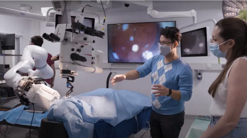 Two people wearing surgical masks standing demonstrating the surgical robot in a high tech operating theatre