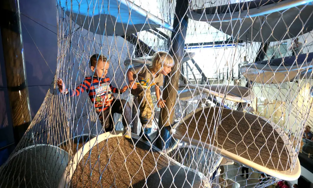 Two children around five years old climbing up oval shaped 'floating' platforms surrounded by protective wire mesh