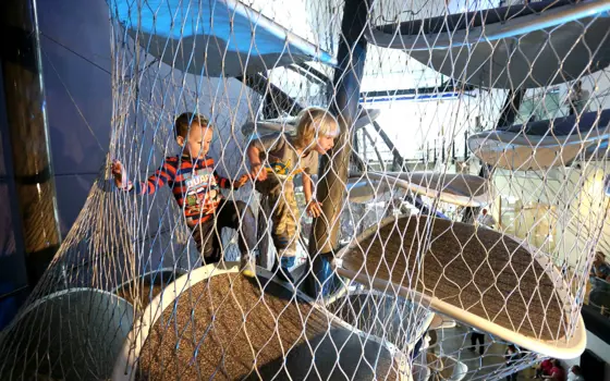 Two children around five years old climbing up oval shaped 'floating' platforms surrounded by protective wire mesh