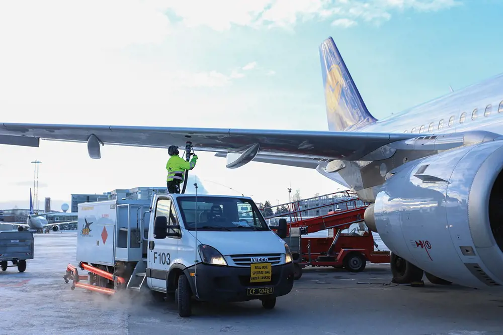 The side of a Lufthansa aircraft with a truck parked under the wing. A person is standing on the truck with a tube that refuels the aircraft from the wing. 