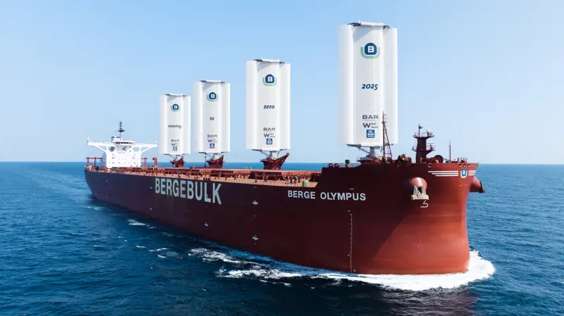 A red container ship viewed from the front, with four white WindWing sails protruding from the deck, producing thrust to save fuel.