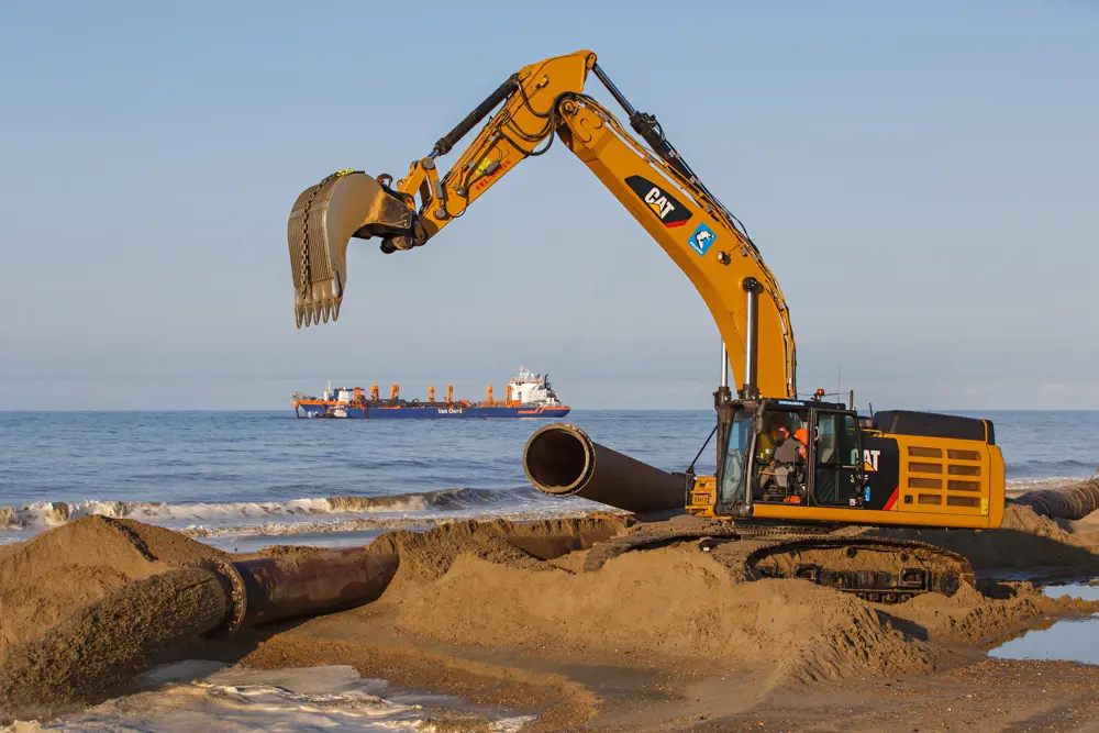 Sand being pumped onto Bacton Beach, with a digger with tracked wheels moving the sand into place.