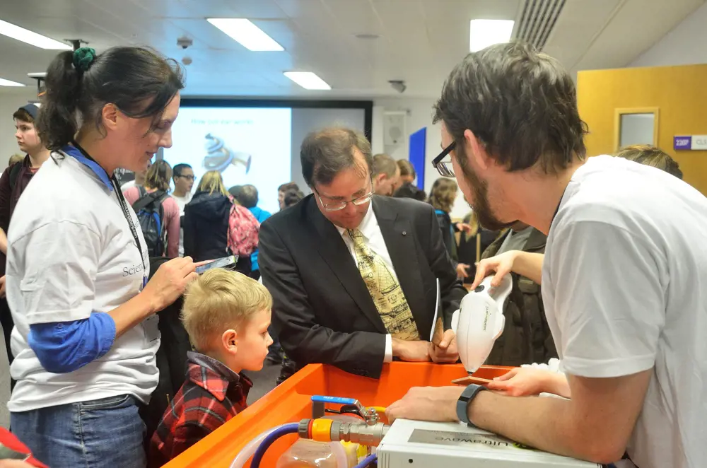 Professor Timothy Leighton engaging in public outreach with children and adults at a stand containing the StarStream device cleaning a surface. 