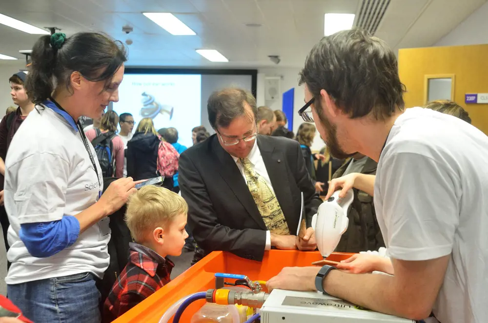 Professor Timothy Leighton engaging in public outreach with children and adults at a stand containing the StarStream device cleaning a surface.