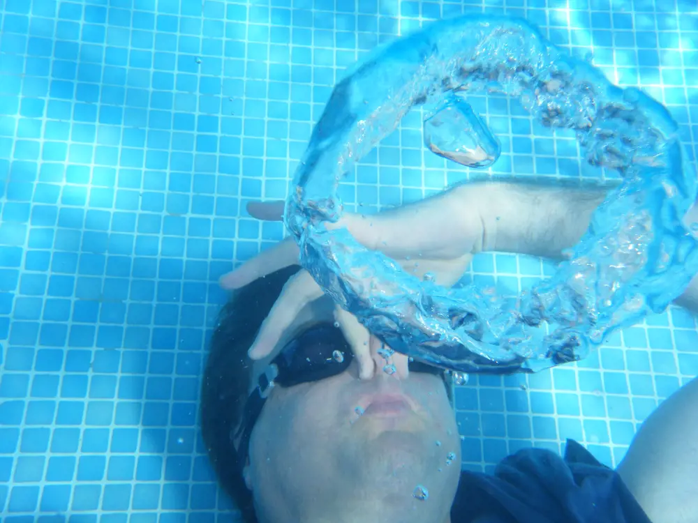 Professor Timothy Leighton lying on the floor of a swimming pool blowing an air bubble ring underwater.