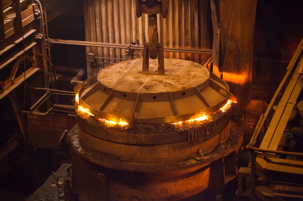 A huge concrete vessel enclosed with a lid, with white-hot molten metal visible in the gap between the lid and the vessel's base and lighting the room with an orange glow..