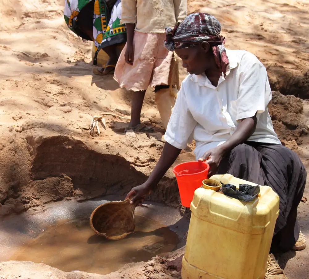 A person scooping out water from a hold in the ground containing water. 