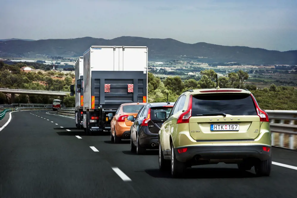 Three cars travelling behind two vans on a road with mountain scenery in front of them.