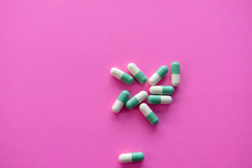 White and green pill capsules on a pink background.