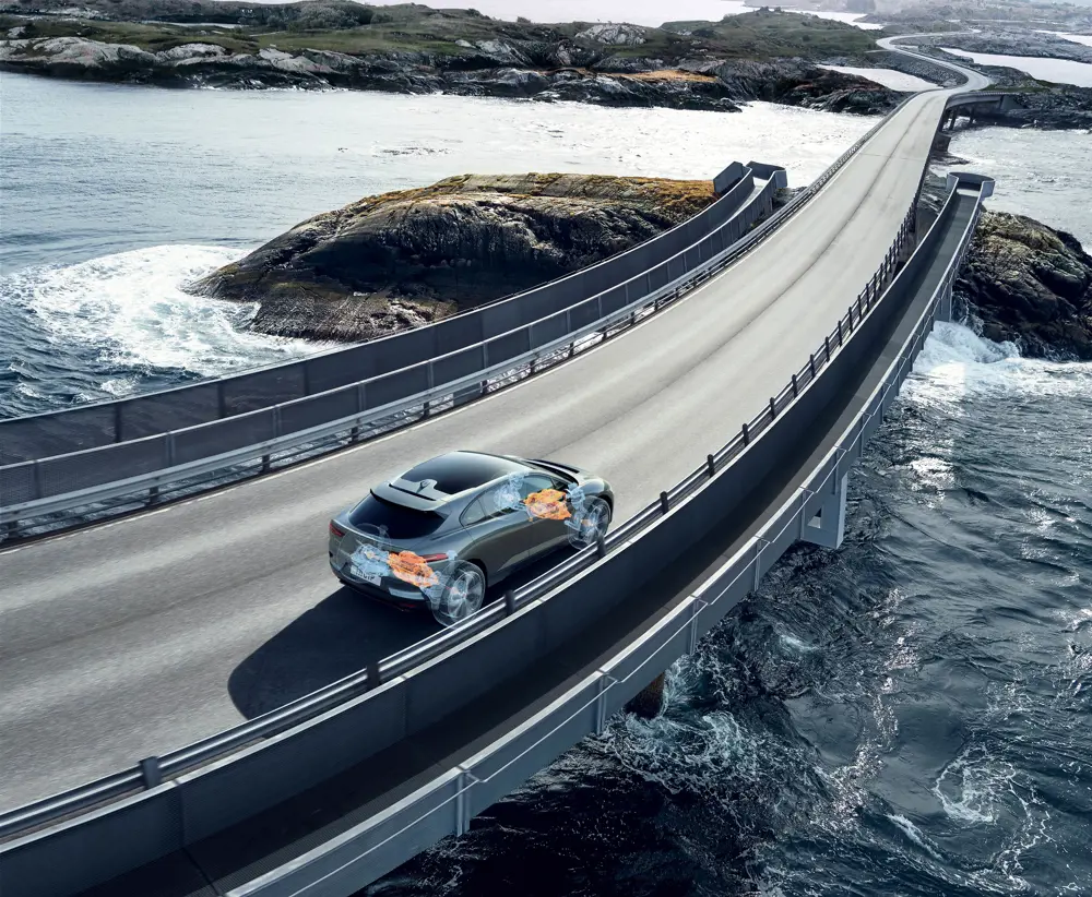 The jaguar I-Pace driving on a bridge across a body of water, with a schematic of the electric parts of the car and the chassis overlaid on the photograph.