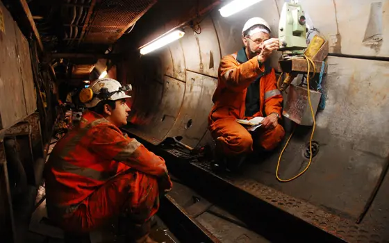 Two tunnel surveyors using equipment inside a tunnel.