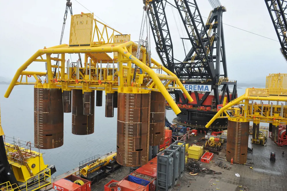 A crane lifting large metal cylinders with the ocean in the background.