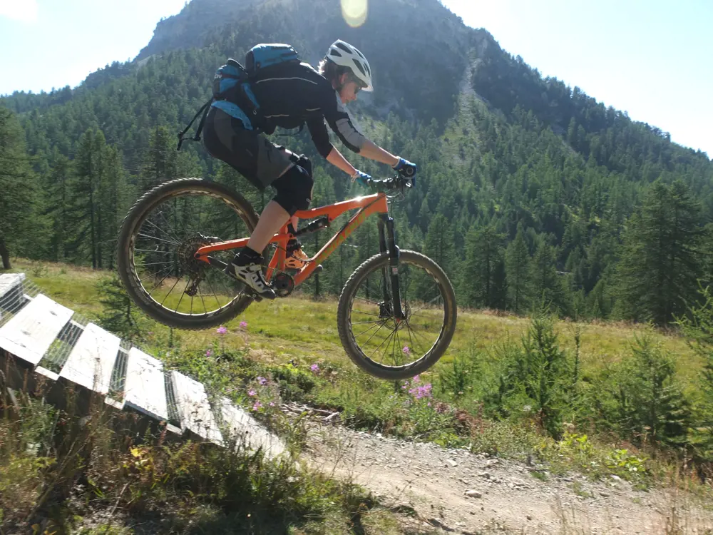 Dr Sarah Williamson FREng on a mountain bike, in the air as the travels down a ramp in the countryside.