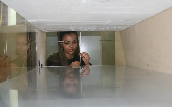 A woman engineer seen through a window in a piece of experimental apparatus, setting up an experiment, holding a thin metal rail