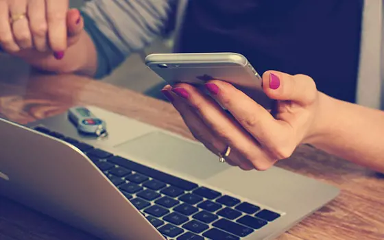 A person holding a phone and using a laptop.