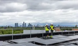 Two engineer colleagues speaking to each other on top of a building with solar panels, with a skyline in the background.