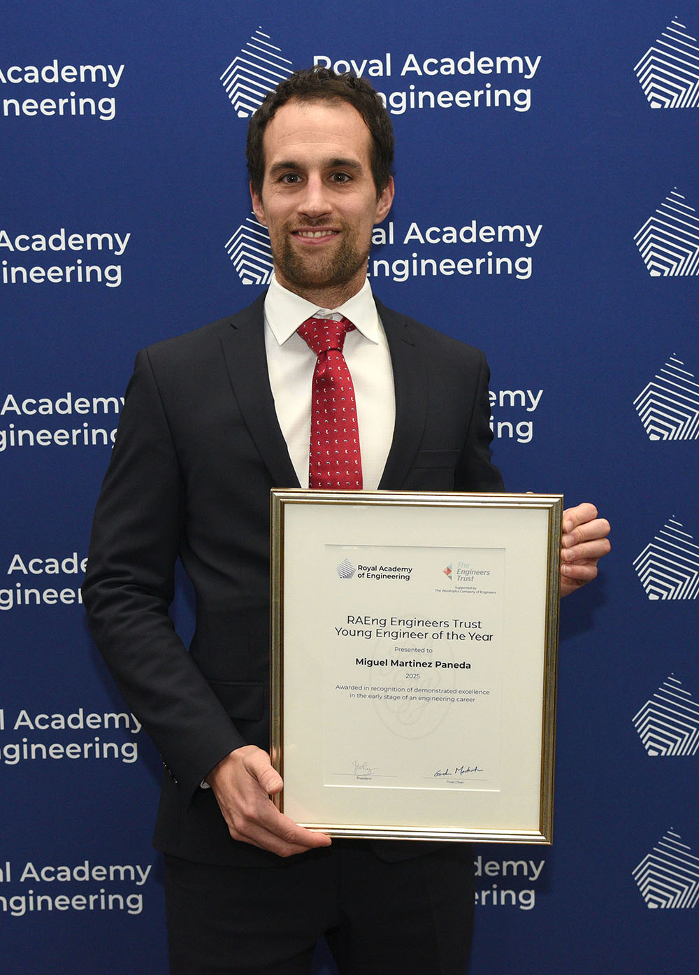 A person in a suit holds an award certificate in front of a Royal Academy of Engineering backdrop.
