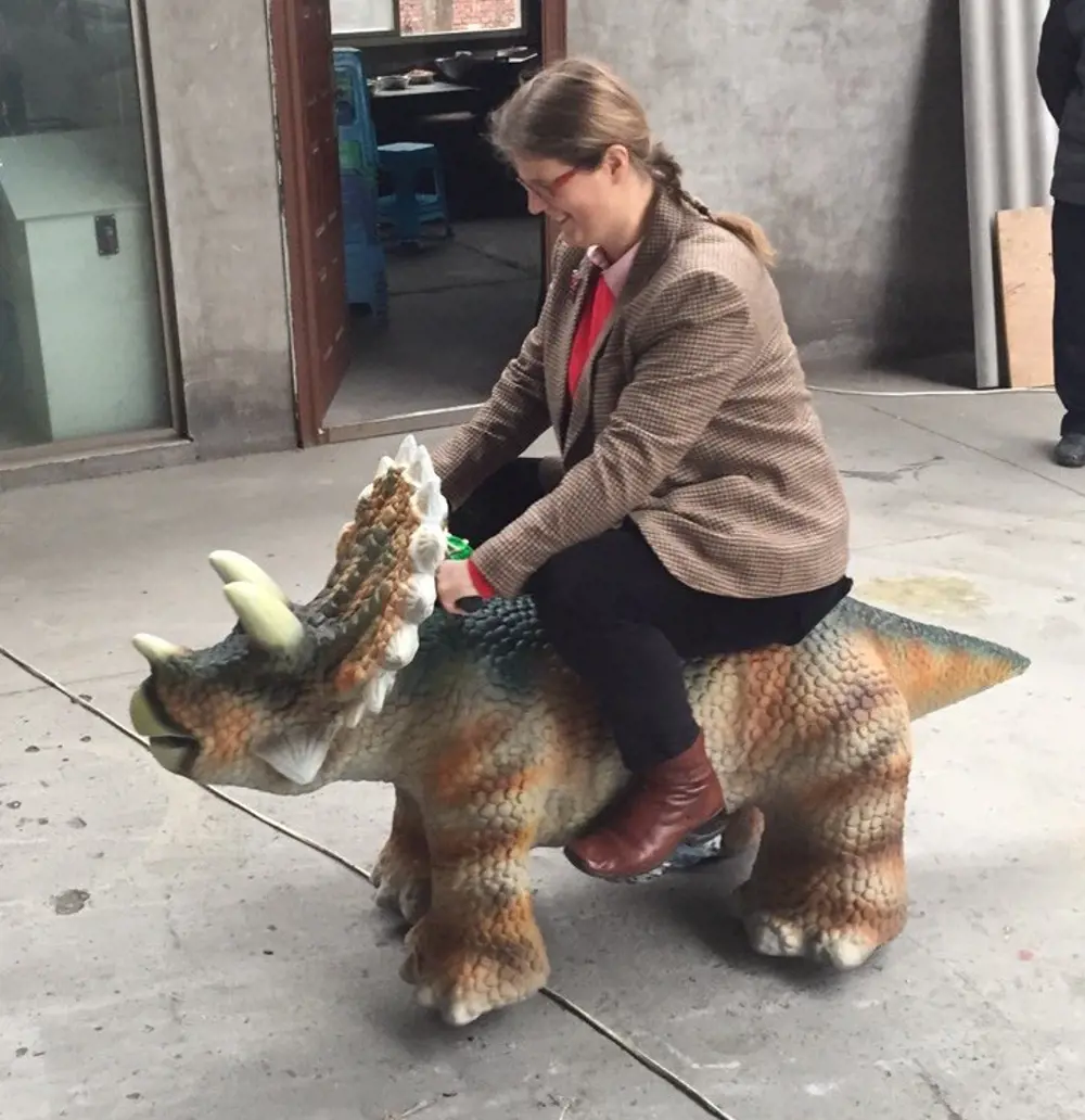 A photograph of Lucy sitting on top of a Triceratops-like dinosaur.