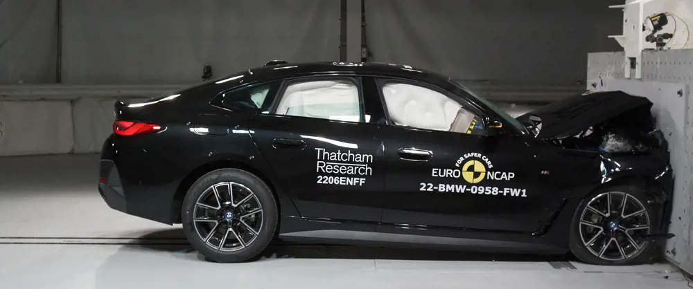 A BMW i4 after hitting a metal wall on its front side during a crash test. The airbags inside have all blown up, and the front of the car has crumpled.