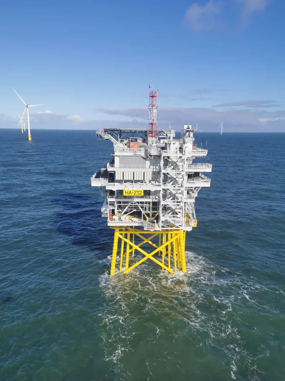 A reactive compensation station in the ocean with wind turbines in the background.