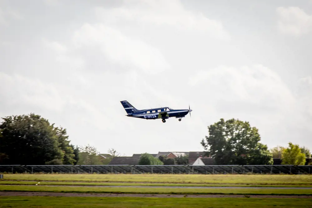 A small 6 seater plane in flight, just after it has taken off from the ground.