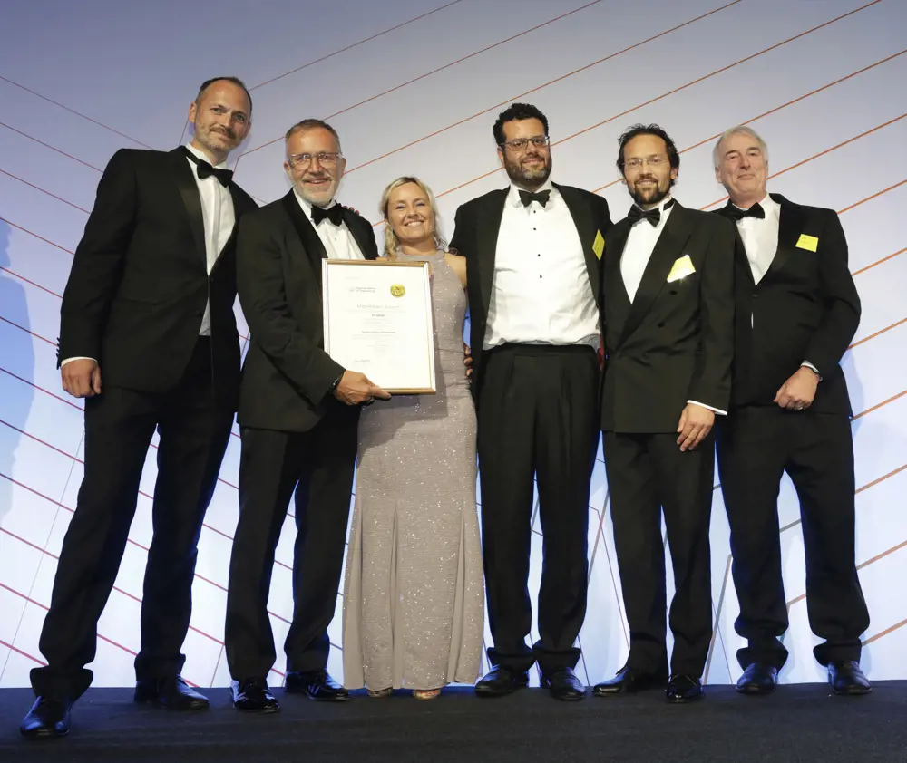 Five men and one woman in smart dress stand on stage with a certificate