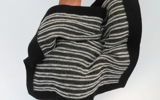 A black fabric woven with over a thousand solar cells, which are seen as a white threaded pattern.