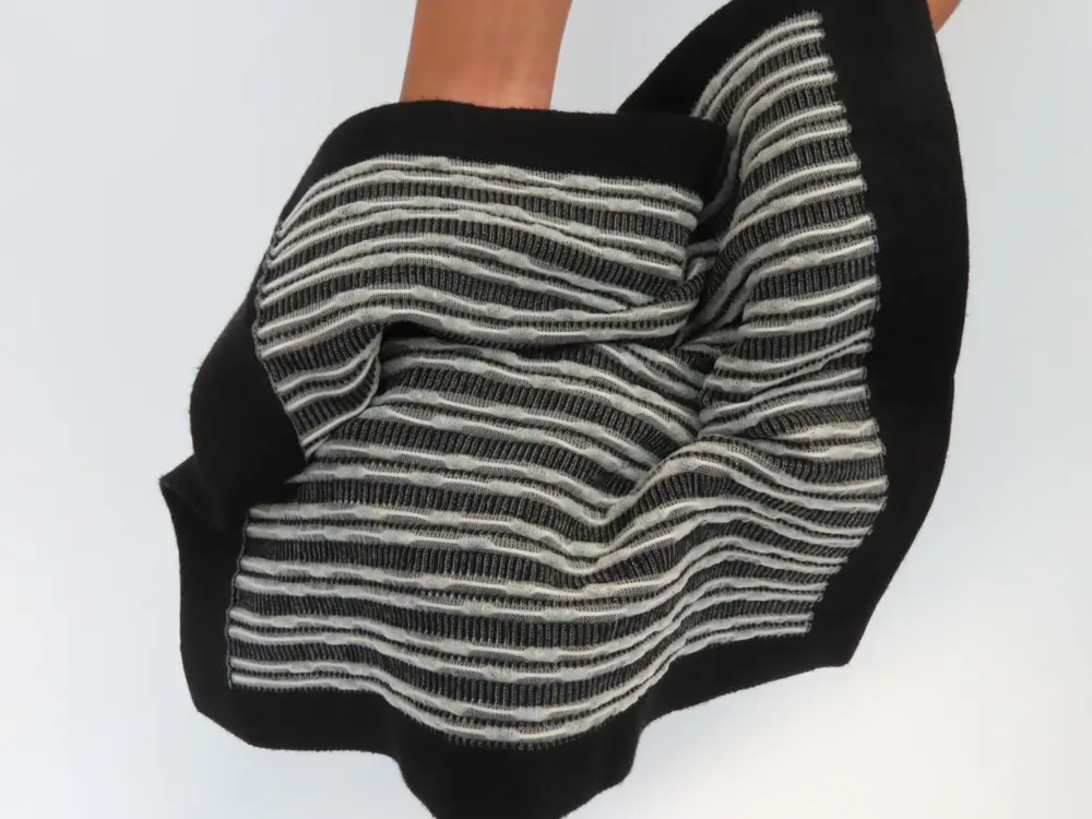 A black fabric woven with over a thousand solar cells, which are seen as a white threaded pattern.