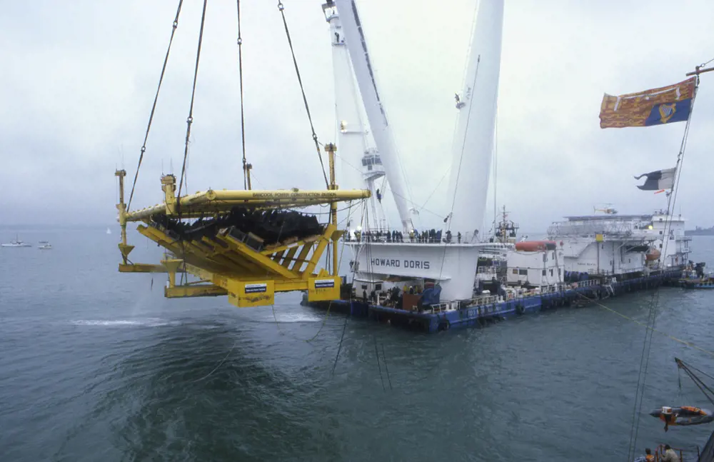 A large crane in the sea lifting a yellow cradle containing the hull of the Mary Rose.