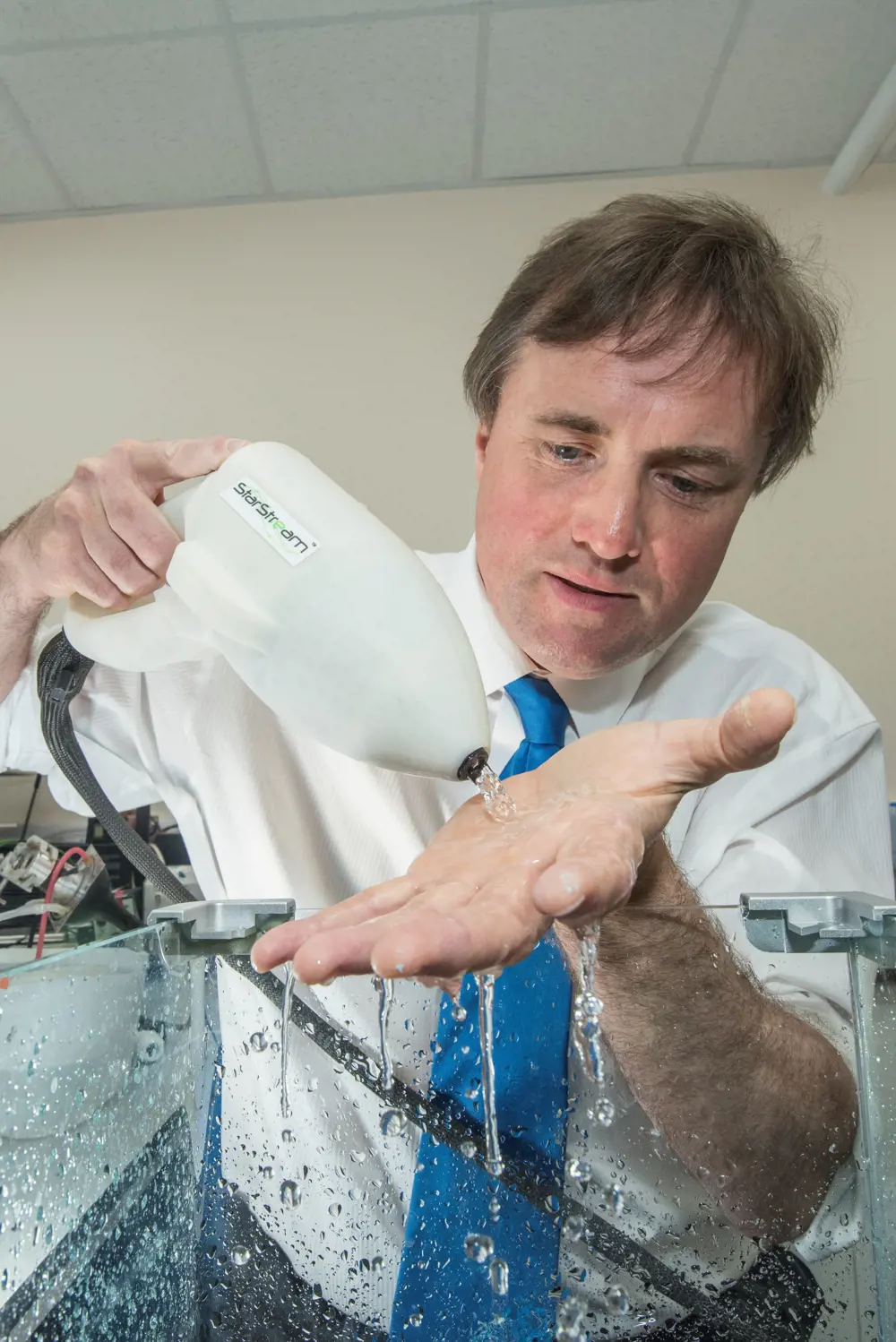 Professor Timothy Leighton using the StarStream device on the open palm of his hand, where the device is letting out clear liquid that is running over his hand.