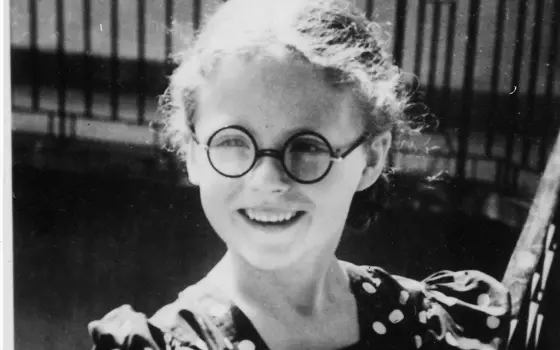 A black and white photograph of a six-year-old girl wearing glasses and a polka dot dress.