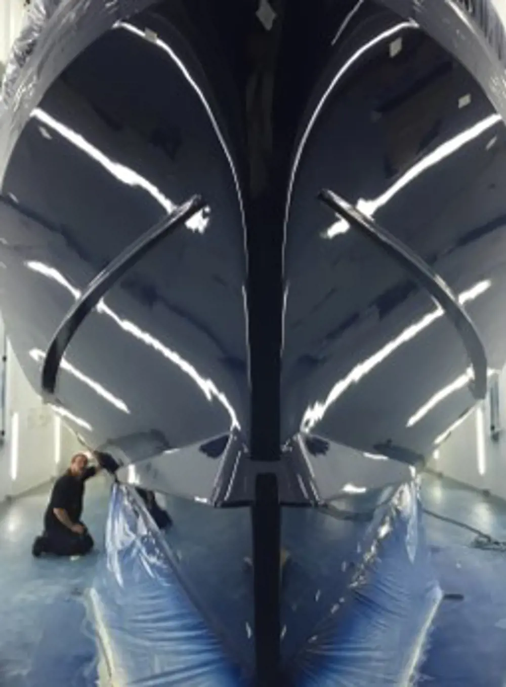 A person kneeling next to the hull of the Shannon boat inside a brightly lit room.
