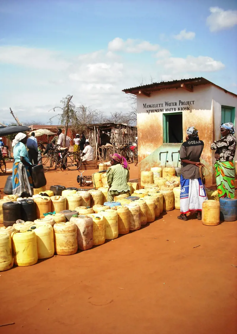 Several people standing outside of a building that has containers with water lined up outside of it.