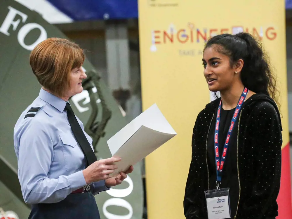 Air Marshal Susan Gray speaking to a young women with an engineering poster in the background.