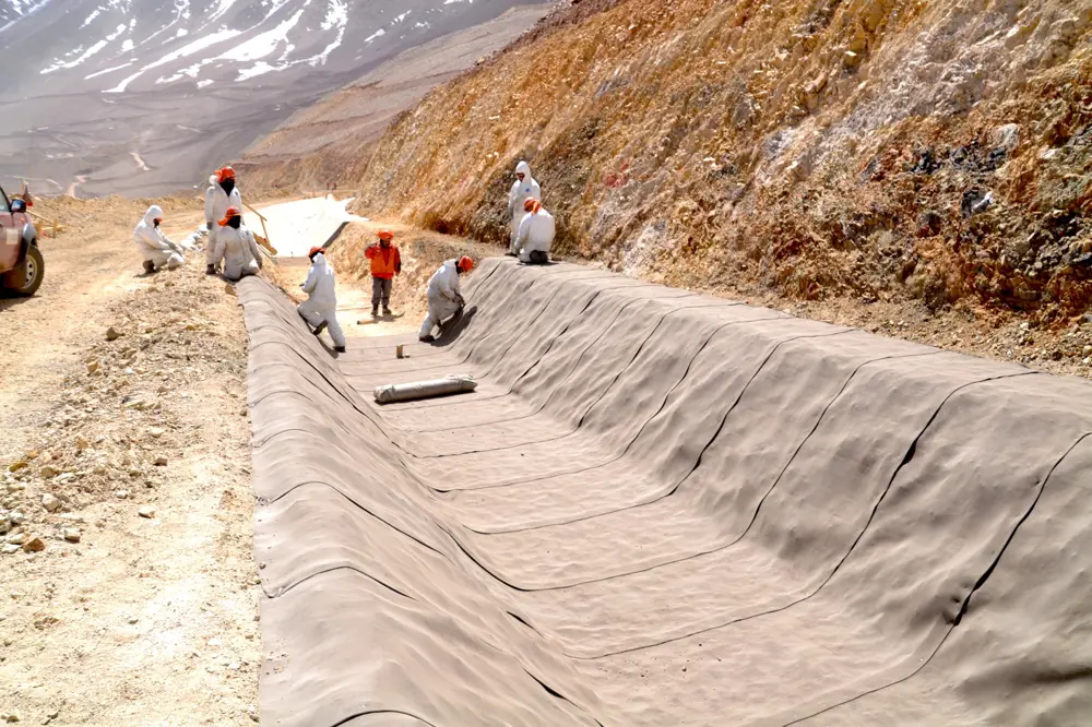 Workers install Concrete Canvas to line a drainage channel in the Atacama Desert, laying the material along a trench cut into a mountainside in a remote mining area.